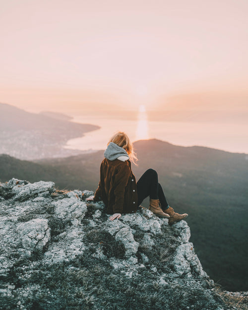 Sugar island CBD newsletter image depicts girl sitting on mountain top with sunrise over a lake in the background