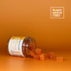 Sugar Island CBD RISE cbd/hemp cbd oil/hemp oil infused gummies; orange gummies spilling out of tipped jar on orange backdrop